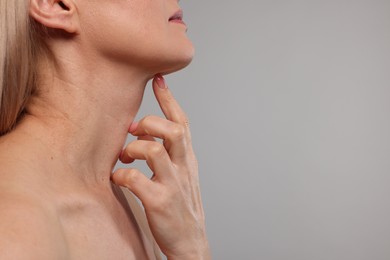 Woman touching her neck on grey background, closeup. Space for text