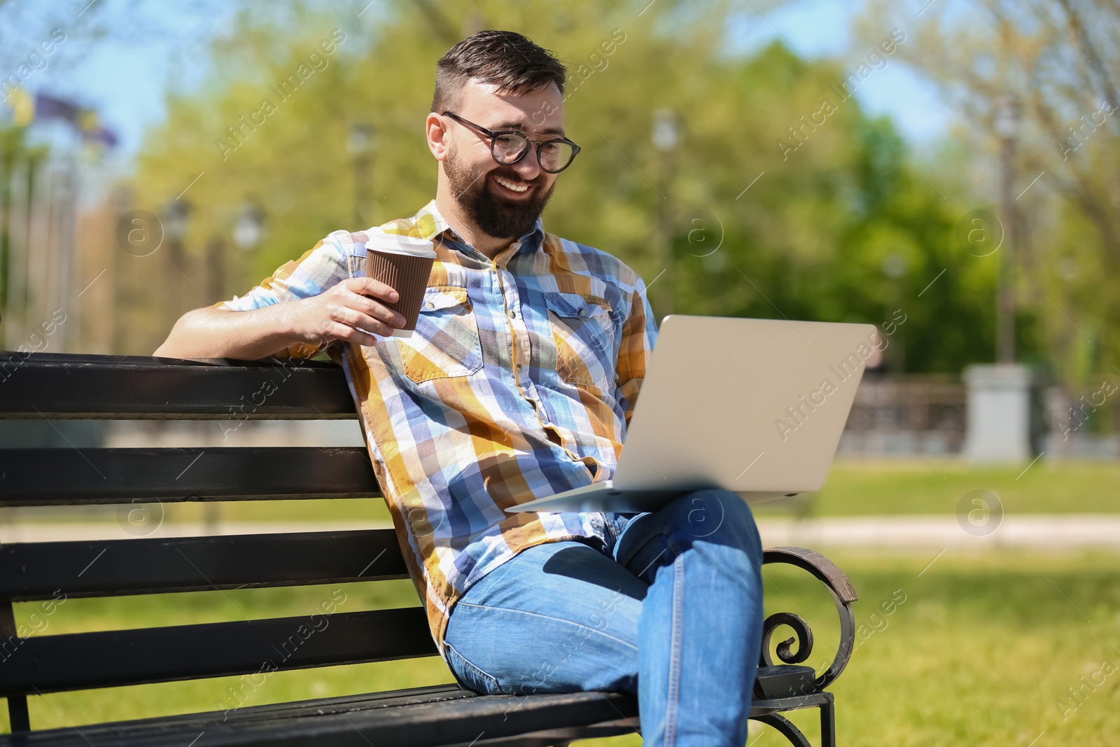 Photo of Portrait of young man with laptop and cup of coffee on bench in park