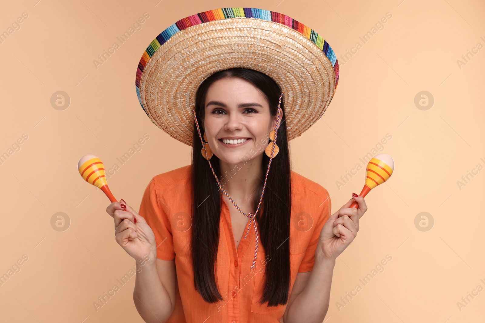 Photo of Young woman in Mexican sombrero hat with maracas on beige background