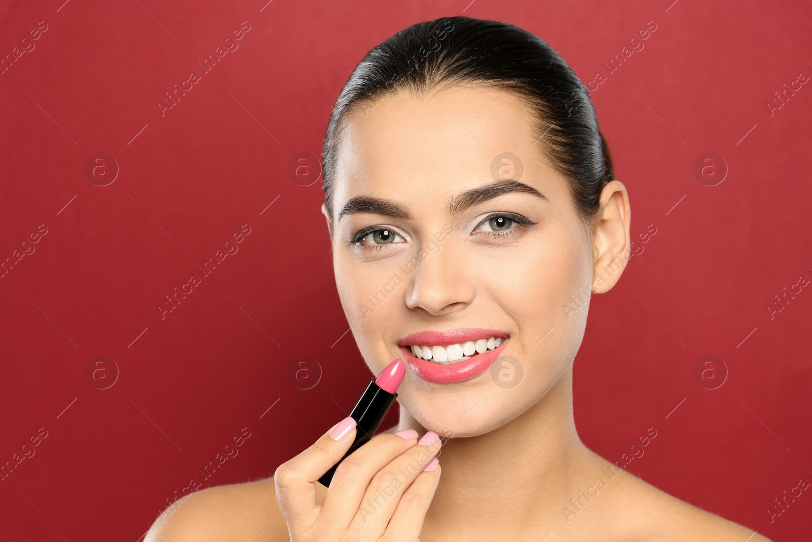 Photo of Young woman applying lipstick on color background