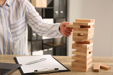 Photo of Playing Jenga. Woman removing block from tower at wooden table in office, closeup