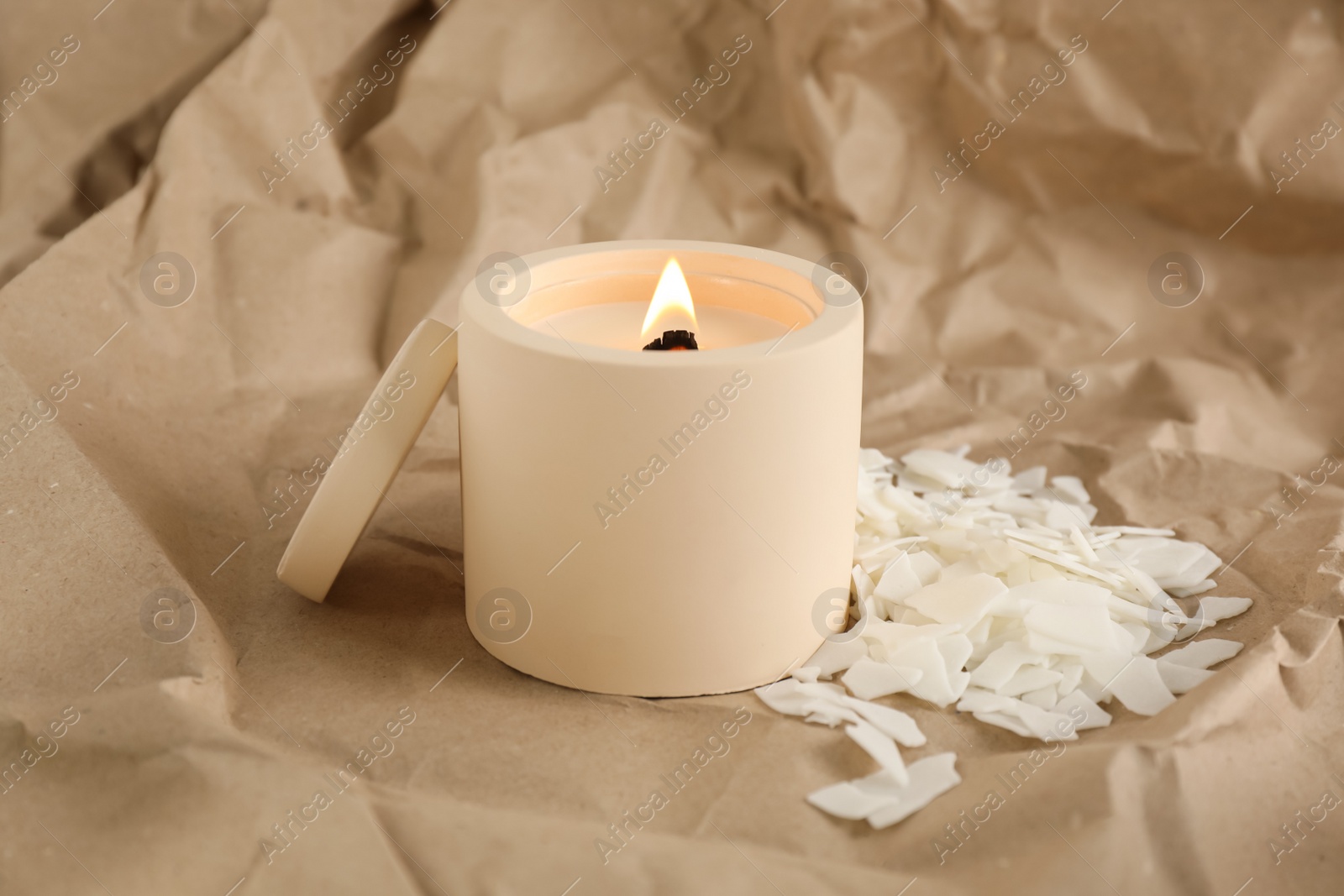 Photo of Burning soy candle and wax flakes on crumpled kraft paper