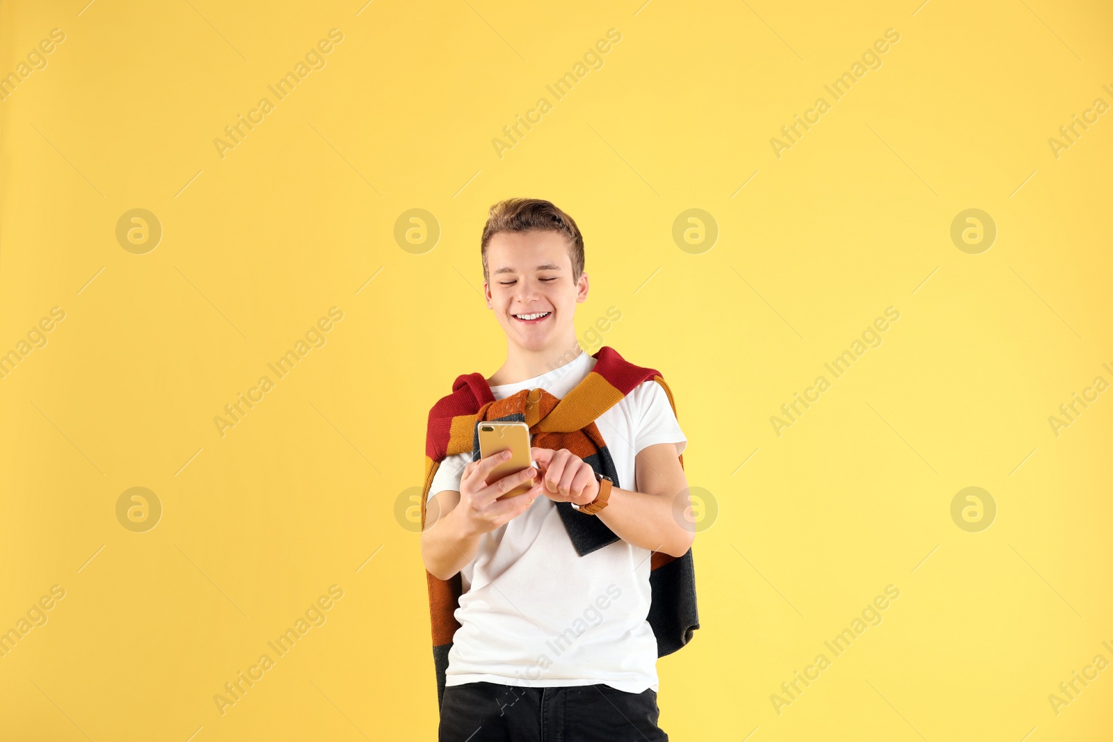 Photo of Handsome teenage boy using mobile phone on color background