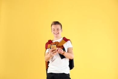Handsome teenage boy using mobile phone on color background