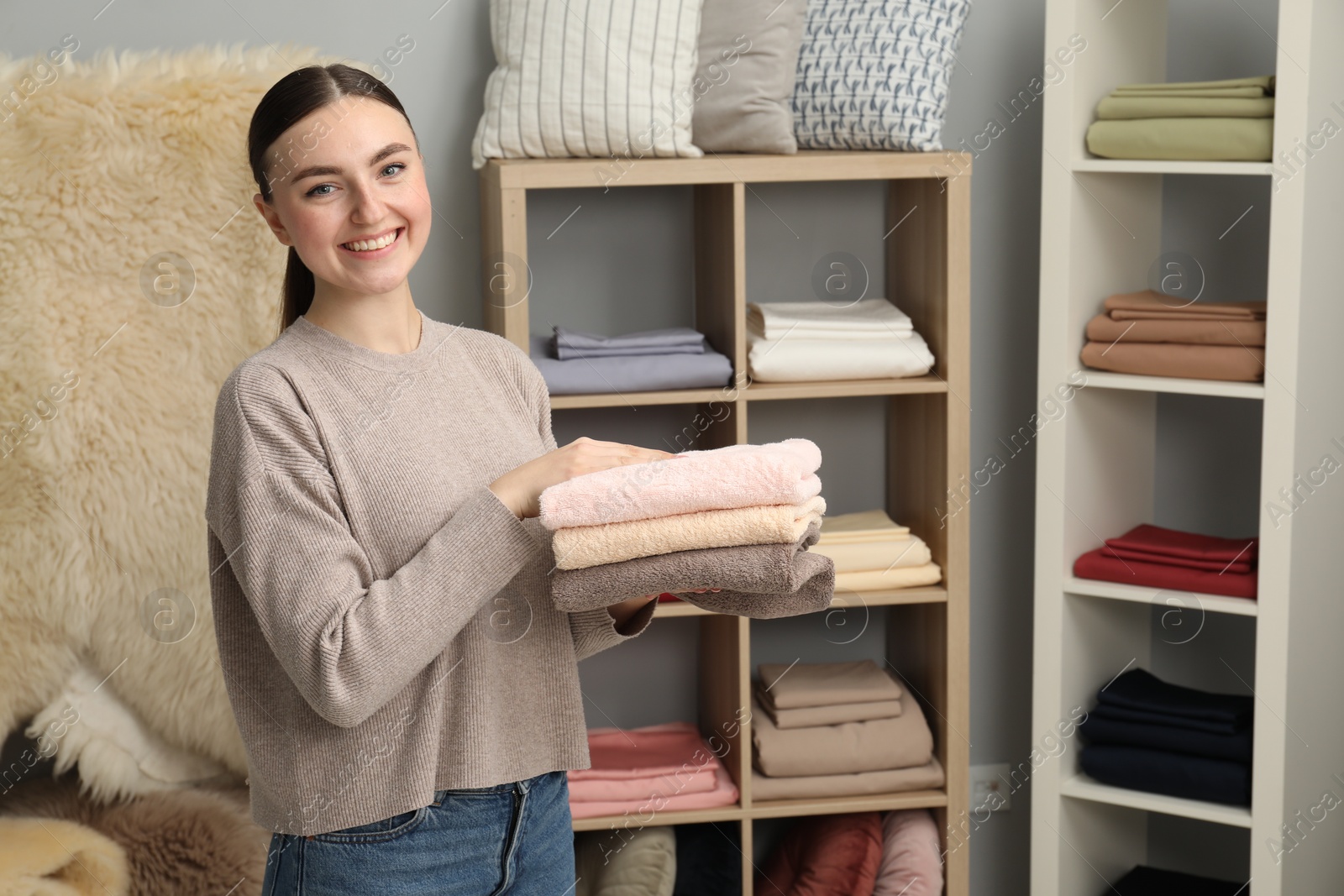 Photo of Smiling young woman holding stack of towels in home textiles store. Space for text