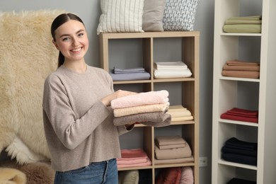 Photo of Smiling young woman holding stack of towels in home textiles store. Space for text