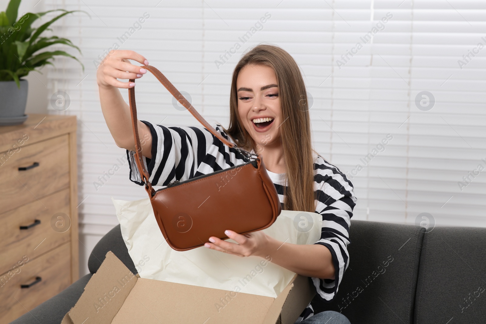 Photo of Happy woman with just unpacked new bag at home. Online store