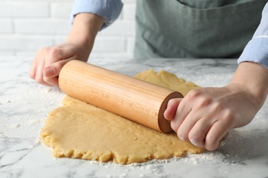 Making shortcrust pastry. Woman rolling raw dough at white marble table, closeup