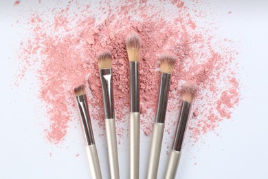 Photo of Makeup brushes and scattered eye shadow on white background, flat lay