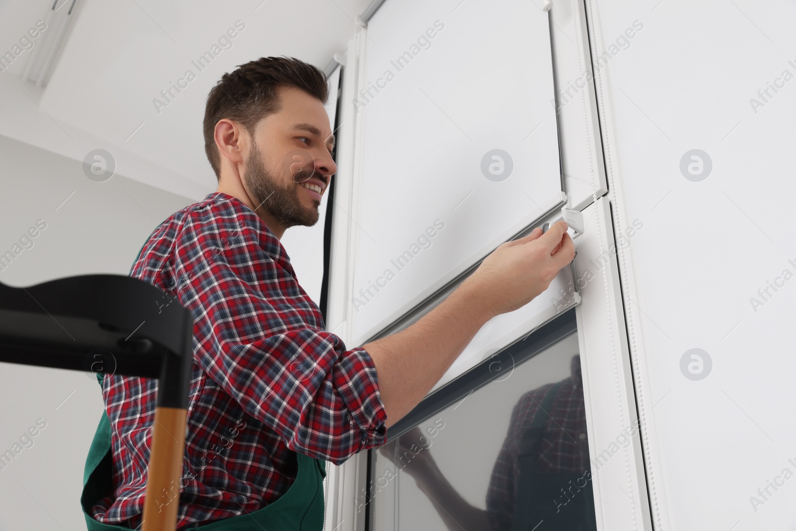 Photo of Worker in uniform installing roller window blind indoors