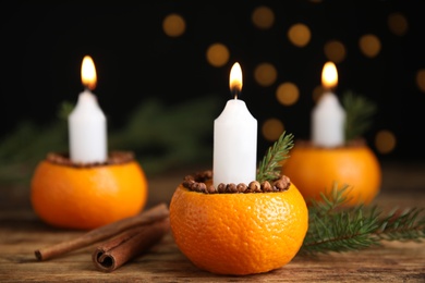 Burning candle in tangerine peel as holder on wooden table against black background