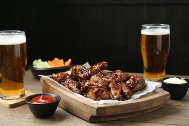 Photo of Tasty chicken wings, sauces, vegetable sticks and glasses of beer on wooden table, space for text. Delicious snacks