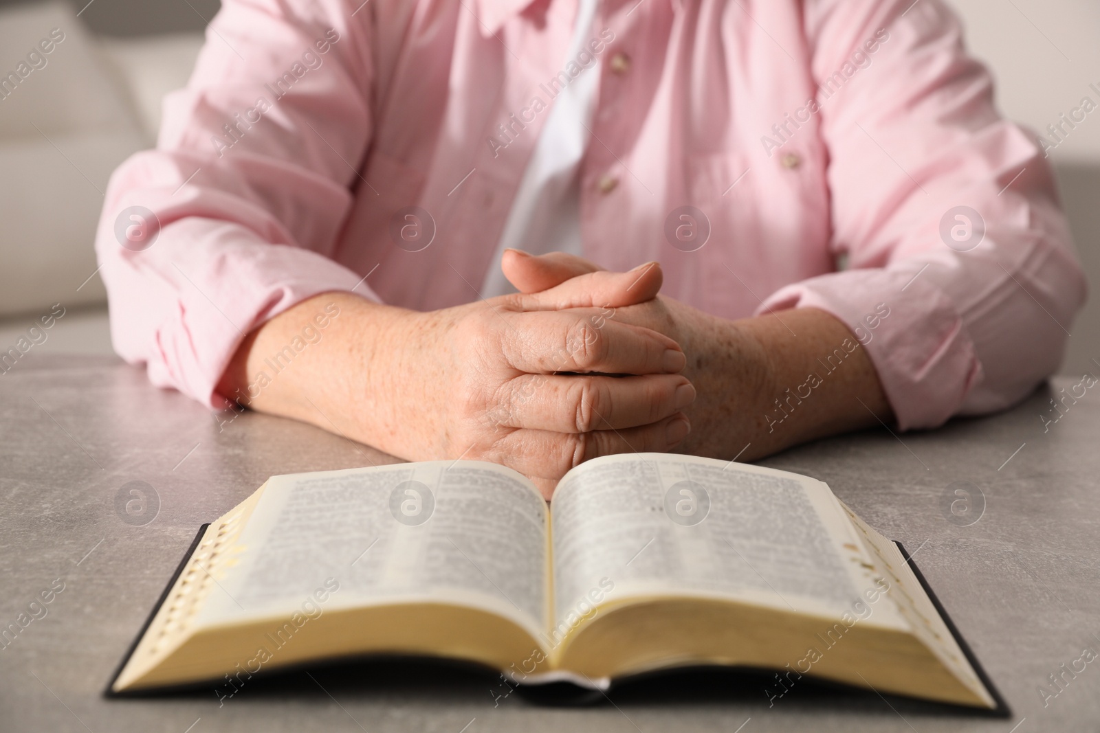 Photo of Mature woman with Bible praying at grey table indoors, closeup