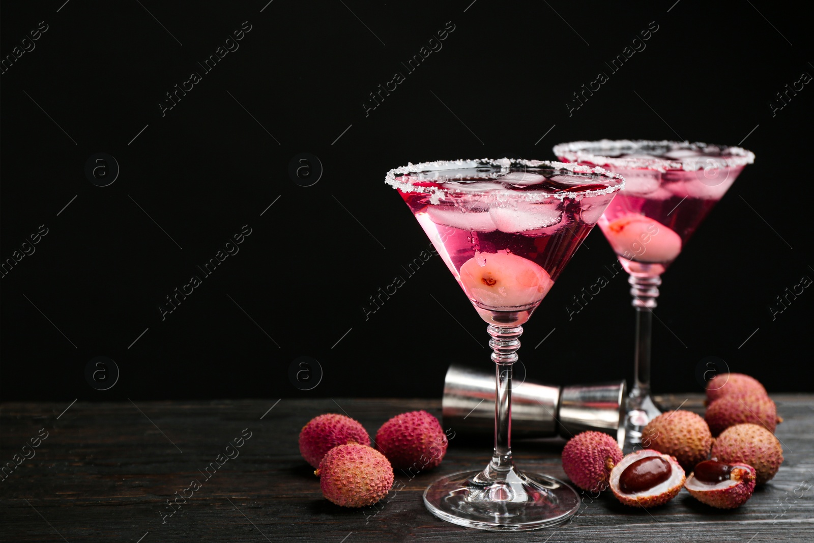 Photo of Lychee cocktail on dark wooden table against black background, space for text