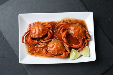 Delicious boiled crabs with sauce and lime on black textured table, top view