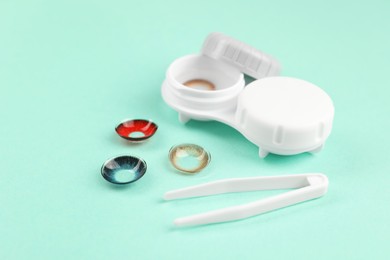 Different color contact lenses, tweezers and case on turquoise background