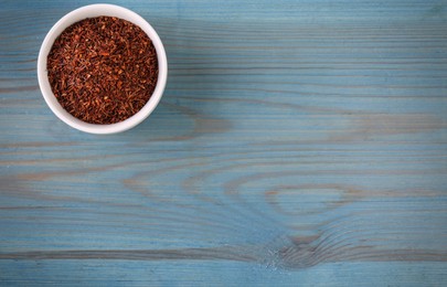 Photo of Dry rooibos leaves in bowl on turquoise wooden table, top view. Space for text