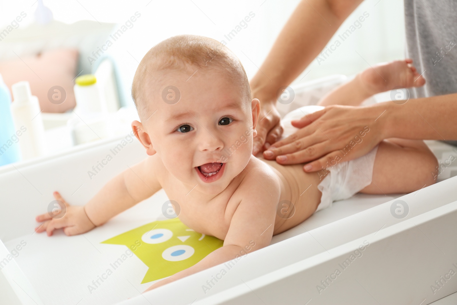 Photo of Young woman massaging cute baby on changing table