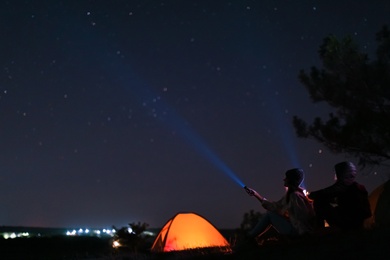Photo of Couple with flashlights near camping tent outdoors at night