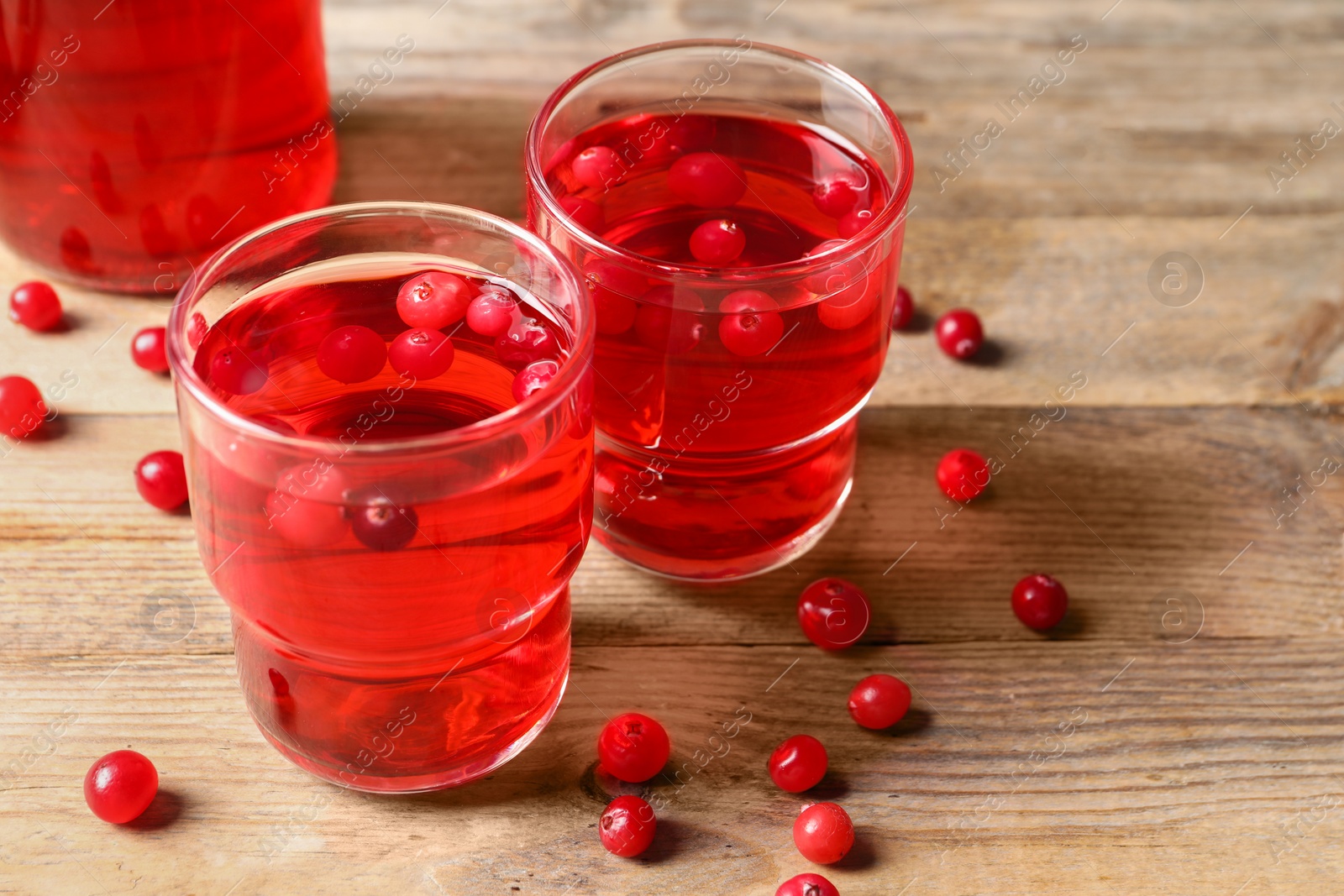 Photo of Tasty cranberry juice in glasses and fresh berries on wooden table, closeup