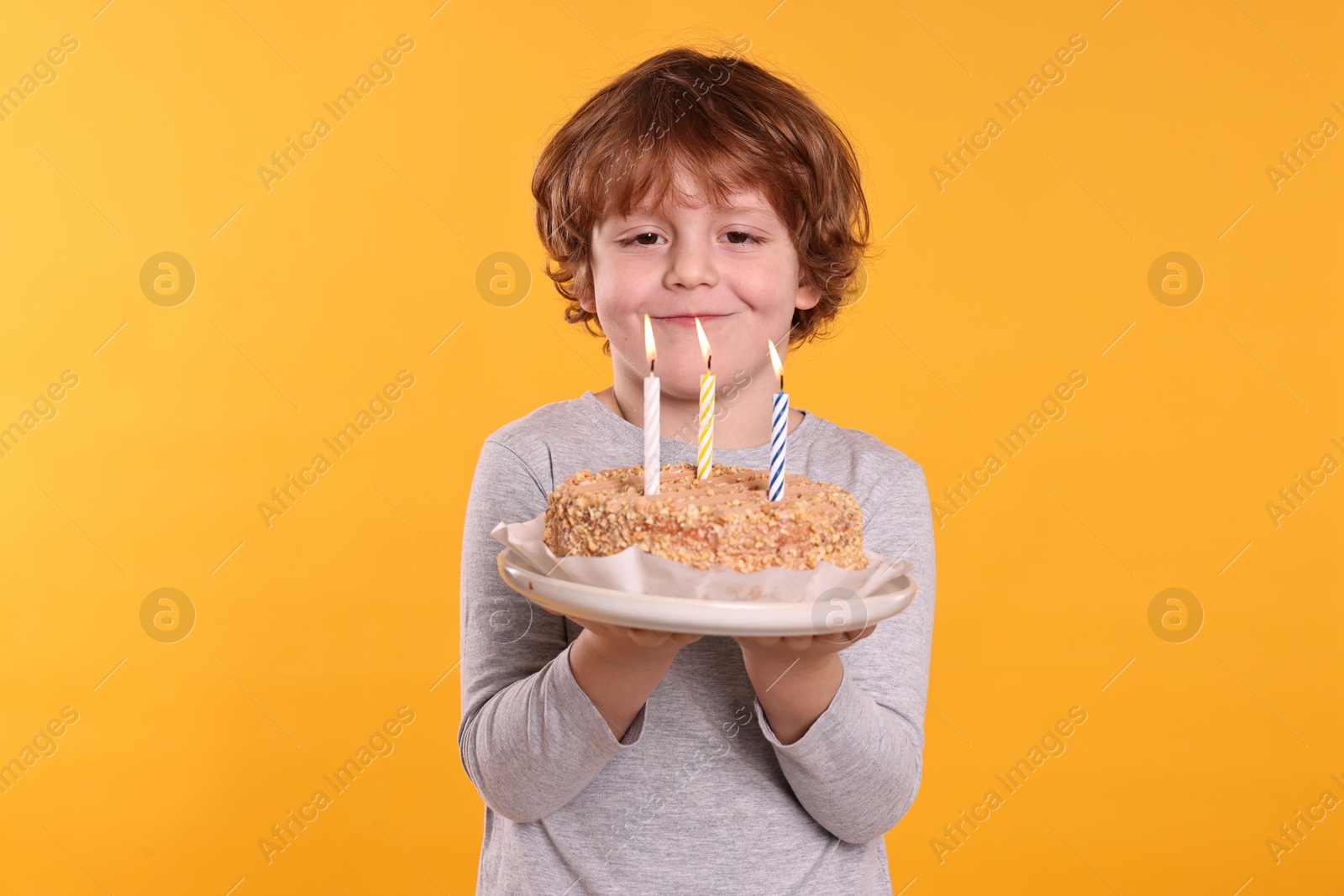 Photo of Birthday celebration. Cute little boy holding tasty cake with burning candles on orange background