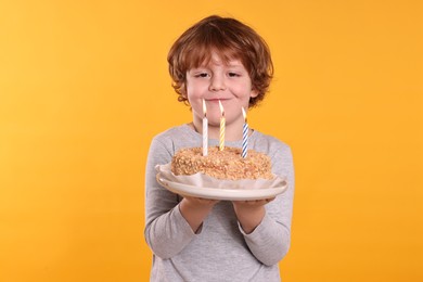 Photo of Birthday celebration. Cute little boy holding tasty cake with burning candles on orange background