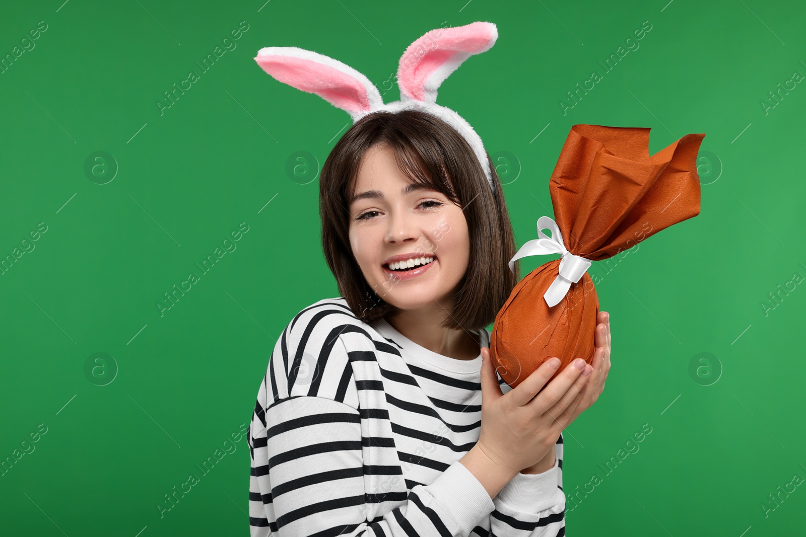 Photo of Easter celebration. Happy woman with bunny ears and wrapped egg on green background