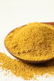 Photo of Curry powder in spoon on white wooden table, closeup
