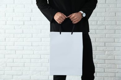 Young man holding paper bag against brick wall, closeup.  Mockup for design