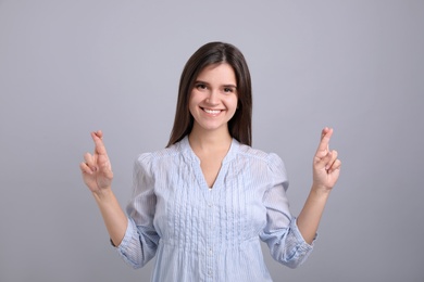 Photo of Happy young woman crossing fingers on grey background. Dealing with stress