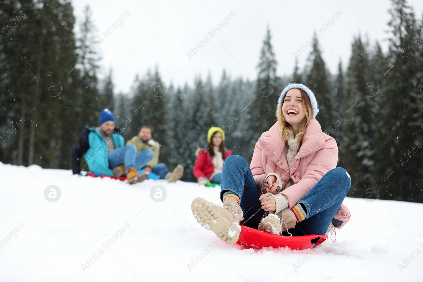 Photo of Happy friends sliding on sleds outdoors. Winter vacation