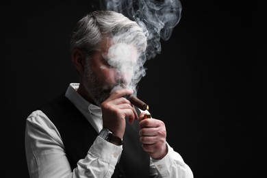 Photo of Bearded man lighting cigar on black background. Space for text