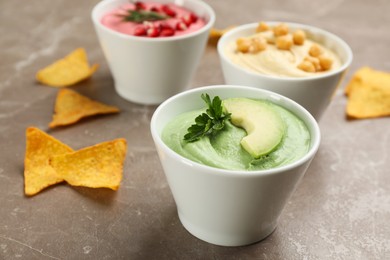 Bowl of delicious green hummus with avocado and parsley on brown marble table