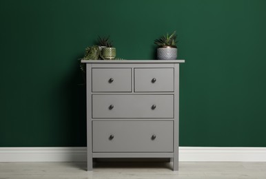 Photo of Modern chest of drawers with houseplants near green wall indoors