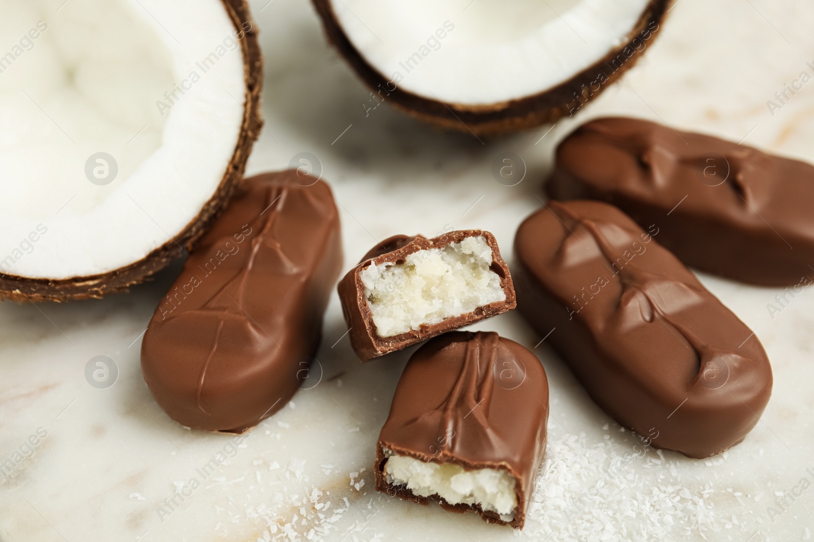 Photo of Delicious milk chocolate candy bars with coconut filling on white table, closeup