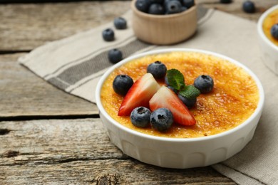 Photo of Delicious creme brulee with berries and mint in bowl on wooden table, closeup. Space for text