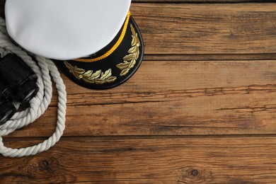 Peaked cap, rope and binoculars on wooden background, flat lay. Space for text