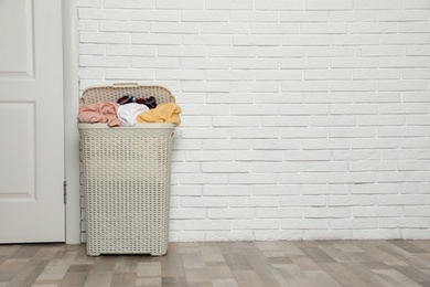 Photo of Plastic laundry basket full of dirty clothes near brick wall in room. Space for text