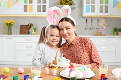 Photo of Mother and her cute daughter with wicker basket full of Easter eggs in kitchen