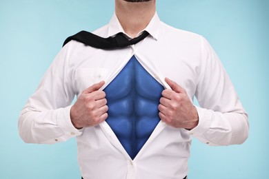 Image of Businessman wearing superhero costume under suit on light blue background, closeup