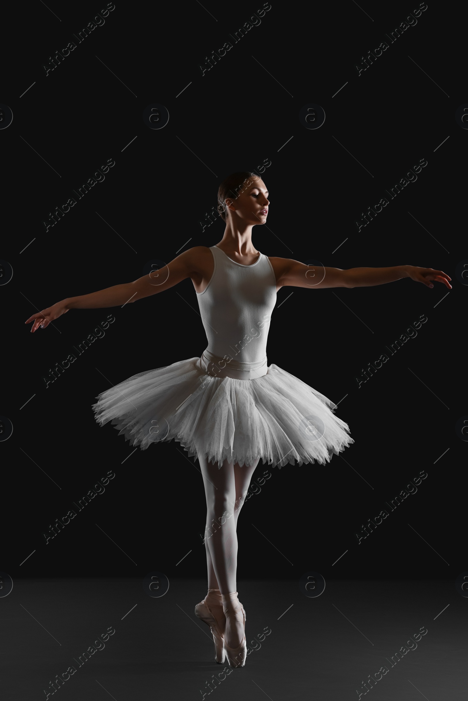 Photo of Young ballerina practicing dance moves on black background