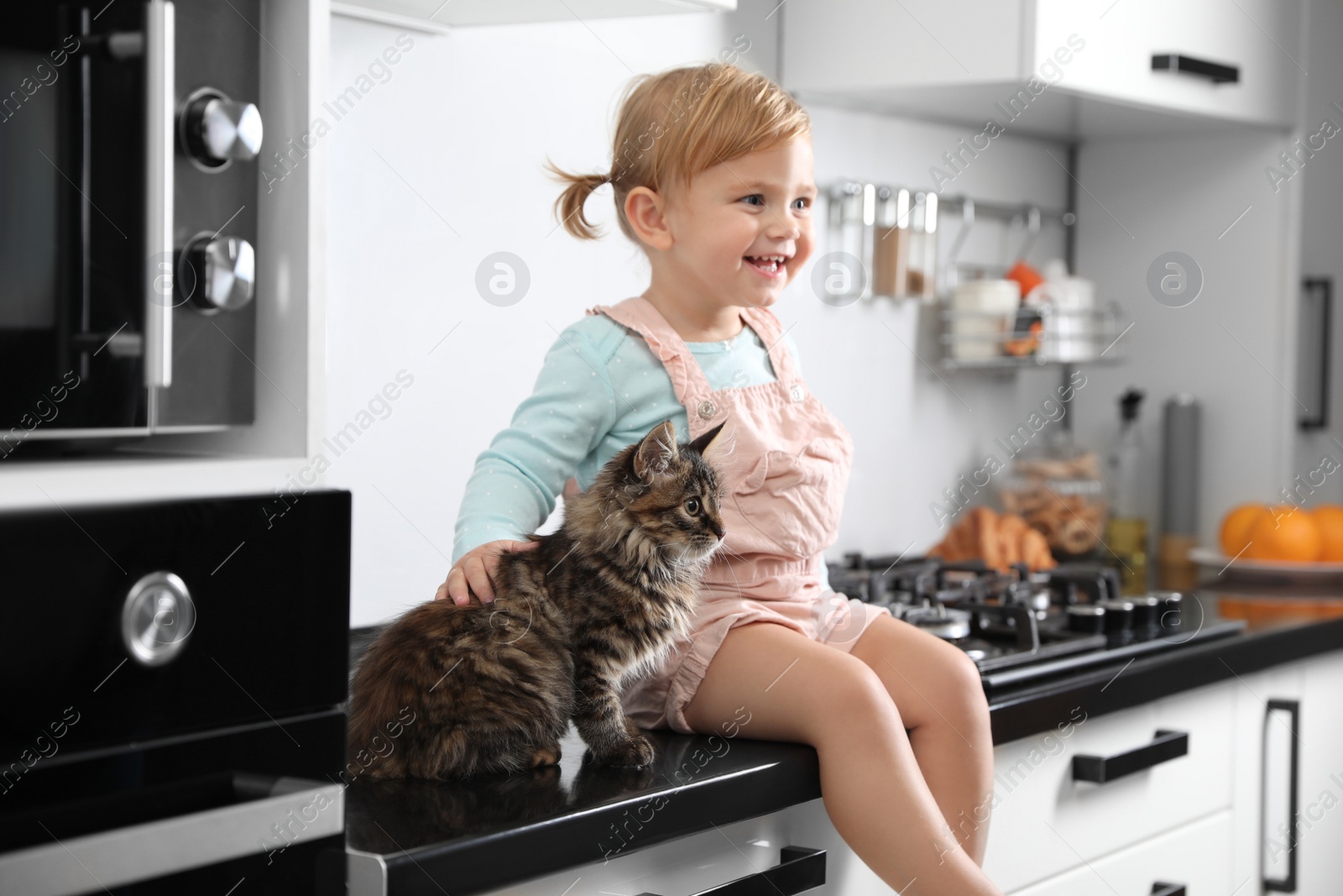 Photo of Cute little child sitting with adorable pet on countertop in kitchen