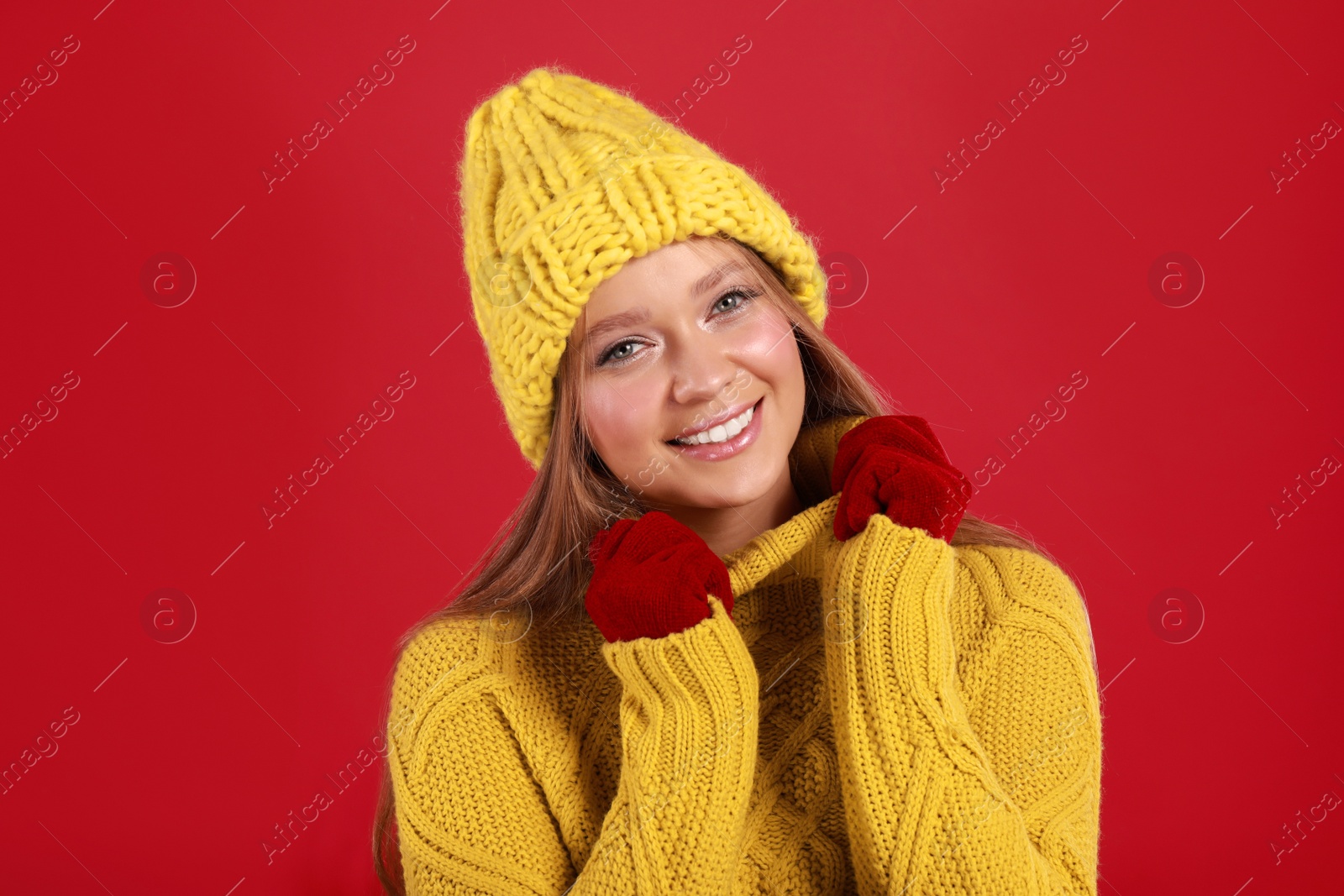 Photo of Young woman in warm sweater, gloves and hat on red background. Winter season