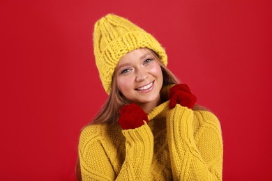 Photo of Young woman in warm sweater, gloves and hat on red background. Winter season