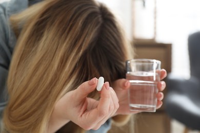 Photo of Young woman with abortion pill and water indoors, focus on hand