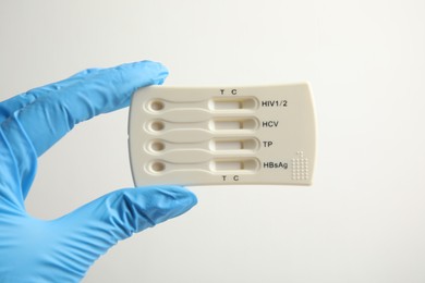 Photo of Doctor in gloves holding disposable express test for hepatitis on white background, closeup