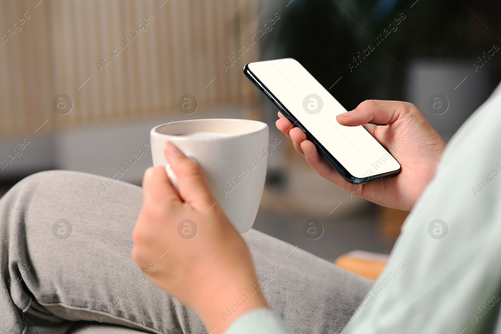 Photo of Woman with smartphone and cup of coffee indoors, closeup