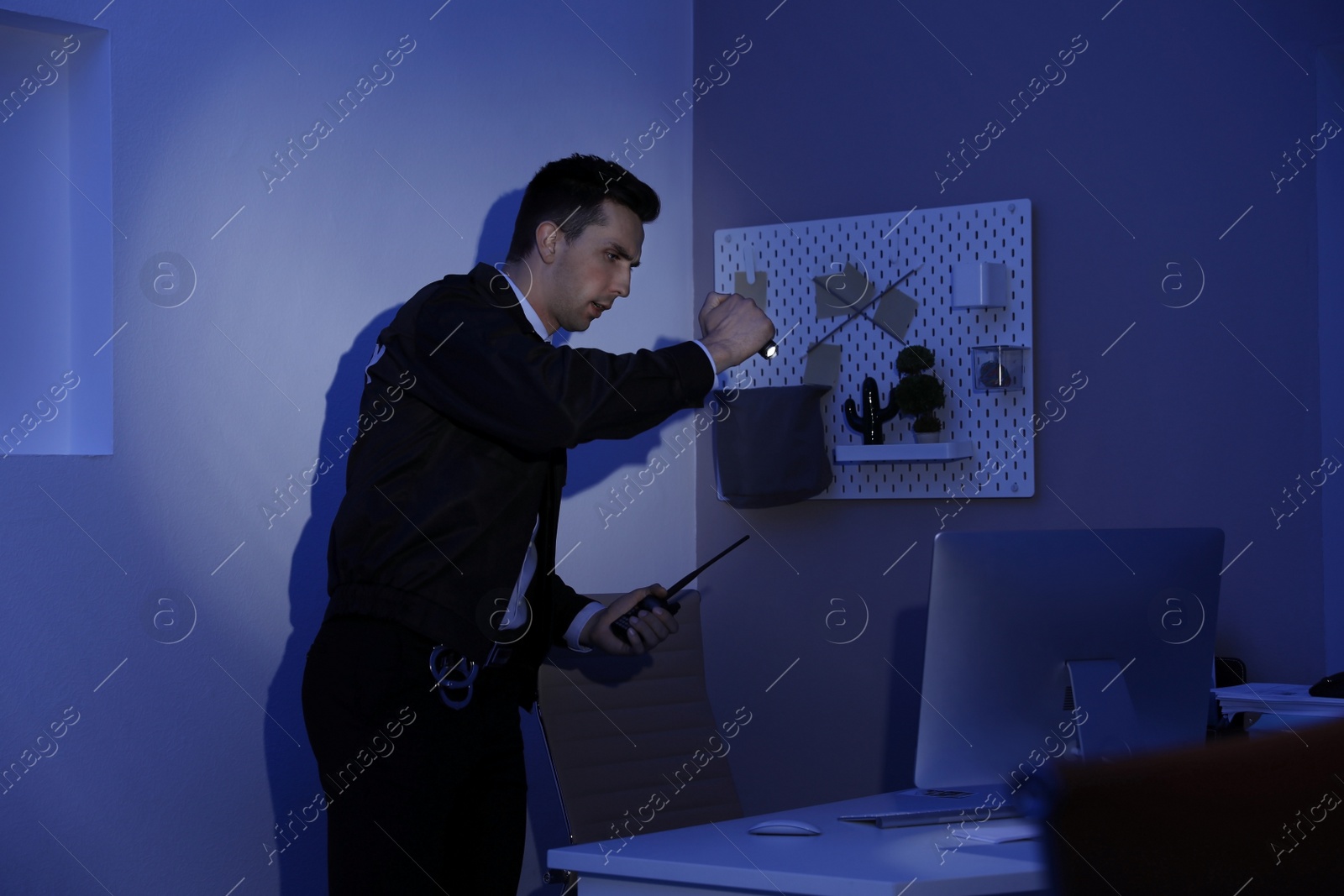 Photo of Male security guard with flashlight and portable radio transmitter in dark room