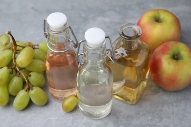 Different types of vinegar and fresh fruits on grey table