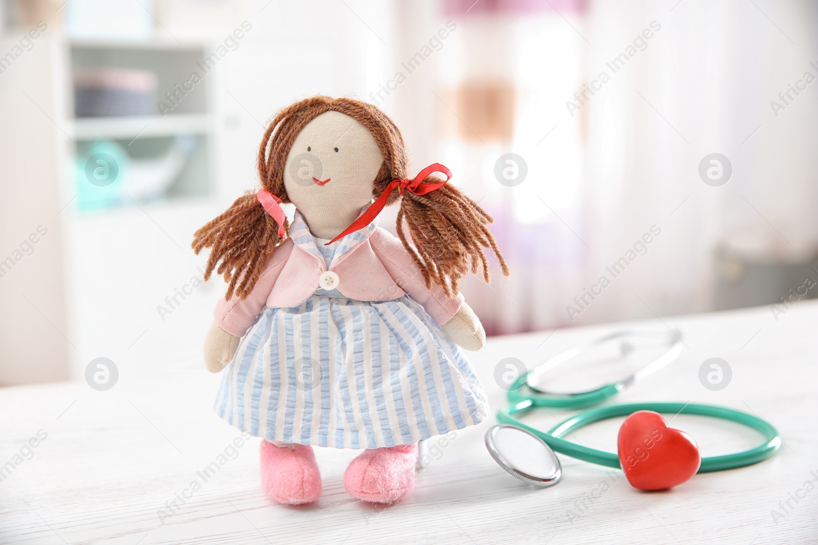 Photo of Doll, stethoscope and heart on table indoors. Children's doctor